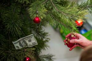 een kind siert een Kerstmis boom met rood speelgoed en dollars foto