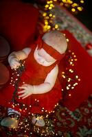 weinig meisje in rood jurk tegen achtergrond van Kerstmis boom houdt Kerstmis slinger in haar handen. baby 6 maand oud viert kerstmis. foto