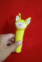 een hand- Holding een geel giraffe vormig baby Holding speelgoed- dat maakt een geluid wanneer geperst. Aan een rood achtergrond foto