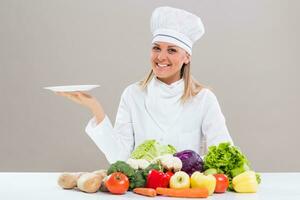 vrouw chef omringd met groenten Holding bord. foto