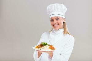 mooi vrouw chef is tonen bereid maaltijd Aan grijs achtergrond. foto