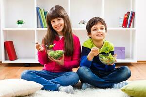 twee kinderen zittend Aan de verdieping en aan het eten groenten foto