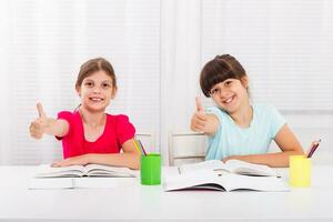 schattig weinig meisjes aan het doen huiswerk samen en tonen duimen omhoog foto