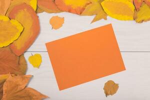 herfst bladeren en geel papier Aan houten tafel foto