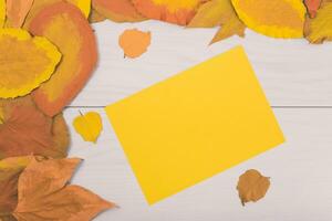 herfst bladeren en geel papier Aan houten tafel foto