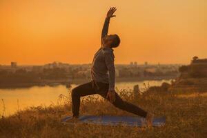 Mens aan het doen yoga Aan zonsondergang met stad visie foto