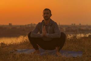 Mens aan het doen yoga Aan zonsondergang met stad visie foto