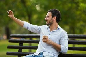 jong zakenman is resting Bij de parkeren, nemen selfie en drinken koffie foto