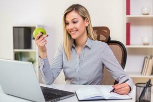 zakenvrouw aan het eten appel terwijl werken in haar kantoor foto