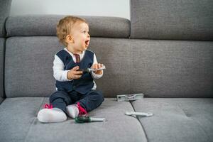 schattig weinig baby jongen spelen met speelgoed terwijl zittend Aan bank. foto