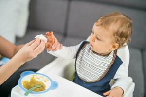 schattig baby jongen kreeg vuil terwijl aan het eten en moeder is schoonmaak hem foto