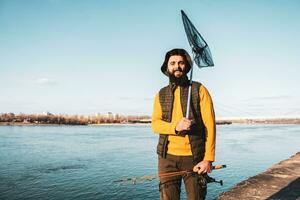 beeld van visser Holding visvangst hengel en visvangst netto terwijl staand door een rivier- foto