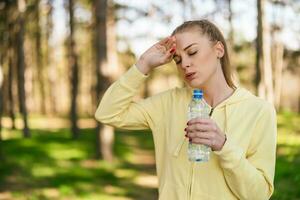 moe vrouw drinken water na oefening in de natuur foto