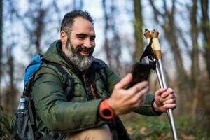 beeld van wandelaar gebruik makend van telefoon terwijl uitgeven tijd in natuur foto