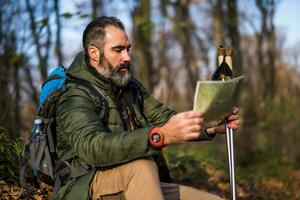 beeld van wandelaar zittend in natuur en op zoek Bij kaart foto