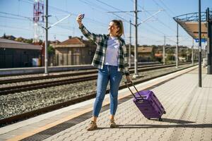gelukkig vrouw is nemen selfie met mobiel telefoon terwijl staand Aan een trein station foto