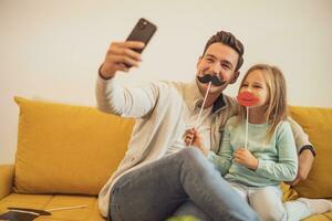 vader en dochter nemen selfie terwijl ze hebben pret met partij rekwisieten Bij hun huis foto
