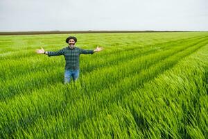 gelukkig boer met armen uitgestrekt staand in zijn groeit tarwe veld- foto
