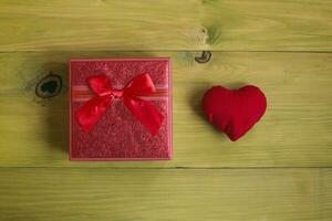 rood geschenk doos met rood lint en hart Aan houten achtergrond foto