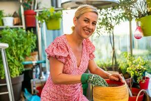 gelukkig vrouw geniet in tuinieren Aan balkon Bij haar huis. ze is zetten bodem in bloem pot. foto