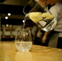 hand- van een onzichtbaar ober gieten van een glas karaf van limonade in een glas. selectief focus. hoog kwaliteit foto