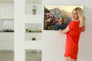 een gelukkig jong blond vrouw is Holding een groot muur canvas Bij huis foto