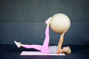 flexibel jong vrouw aan het doen yoga met fit bal in Sportschool terwijl aan het liegen Aan mat foto