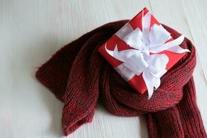 rood geschenk doos geïsoleerd Aan een rood gebreid sjaal met wit houten achtergrond met. kerstmis dag concept. planning het roosteren agenda, evenement, organisator Kerstmis dag. vlak leggen, top visie. foto