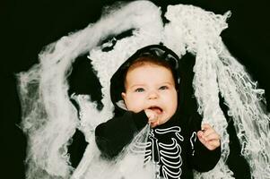 halloween portret van aanbiddelijk baby vervelend skelet kostuum, poseren Aan zwart achtergrond gedekt met spin web foto