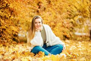 herfst portret van jong gelukkig meisje zittend Aan grond met geel gebladerte achtergrond, gezond levensstijl foto