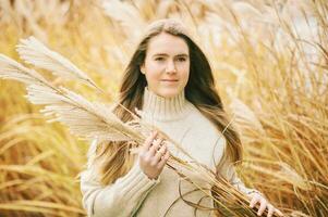 vallen portret van jong mooi meisje poseren buiten met pampa gras, vervelend warm beige stoppen, winderig dag foto