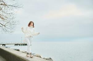 portret van mooi vrouw uitgeven dag buiten door oever van het meer, vervelend wit kleren foto