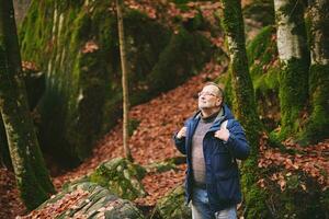 knap midden- leeftijd Mens wandelen in Woud, vervelend warm jasje, rugzak en bril foto