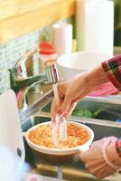 dichtbij omhoog beeld van vrouw handen het wassen linzen in vergiet onder rennen kraan water foto