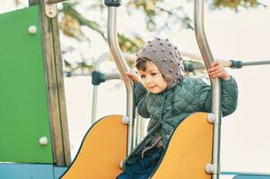 aanbiddelijk kleuter meisje hebben pret Aan speelplaats vervelend warm jasje foto