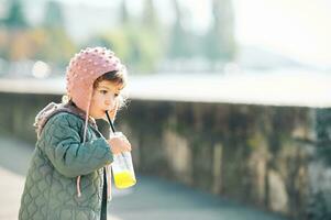 buitenshuis portret van schattig weinig meisje drinken oranje sap Aan haar ochtend- wandelen foto