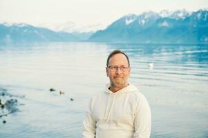 portret van knap Mens bewonderend mooi meer met bergen, vervelend wit sweater foto