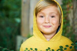 buitenshuis portret van aanbiddelijk 5 jaar oud jongen vervelend geel capuchon foto