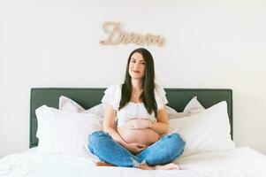 binnen- portret van mooi jong zwanger vrouw resting Aan bed foto