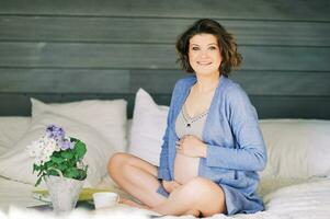 vroeg ochtend- portret van gelukkig jong zwanger vrouw resting in bed, drinken thee foto
