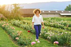 platteland levensstijl, buitenshuis portret van mooi midden- leeftijd 50 - 55 jaar oud vrouw genieten van mooi hoor dag in bloem boerderij tuin foto