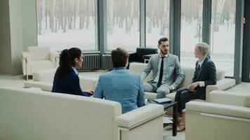 groep van bedrijf partners bespreken overeenkomst zittend Aan bankstel in modern kantoor hal met panoramisch ramen binnenshuis foto