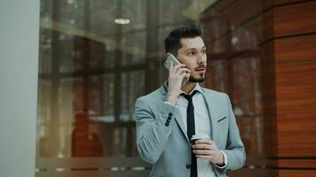 stedicam schot van vrolijk zakenman pratend met smartphone en wandelen in modern kantoor hal binnenshuis foto