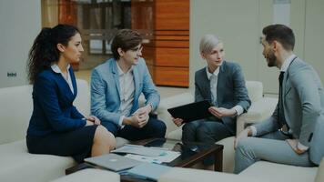zakenvrouw met digitaal tablet pratend met mannetje en vrouw bedrijf collega's zittend Aan bankstel in modern kantoor binnenshuis foto