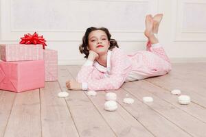 schattig weinig meisje in pyjama- met snoepgoed zittend Aan de verdieping foto