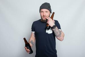 brutaal gebaard mannetje met getatoeëerd arm drankjes een bier van een fles. foto