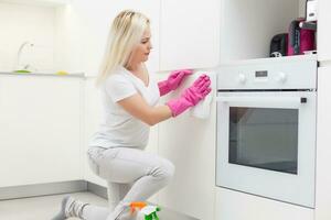 vrouw in de keuken is glimlachen en afvegen stof gebruik makend van een verstuiven en een stofdoek terwijl schoonmaak haar huis, detailopname foto