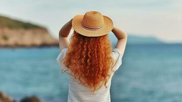 een vrouw met lang krullen haar, aan het bedekken gezicht met hoed Aan kust van blauw zee. generatief ai foto