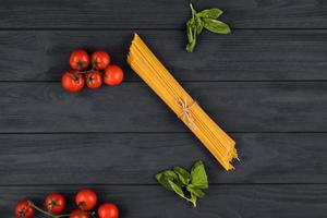 op een donkere achtergrond zijn Italiaanse ingrediënten. pasta, tomaten, basilicum foto