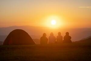 groep van vrienden zittend door de tent gedurende 's nachts camping terwijl op zoek Bij de mooi visie punt zonsondergang over- de berg voor buitenshuis avontuur vakantie reizen concept foto